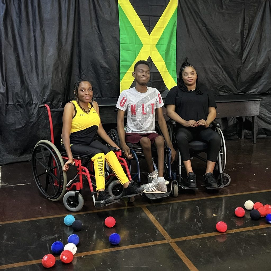 Three Jamaican Boccia players standing in front of the Jamaican flag 